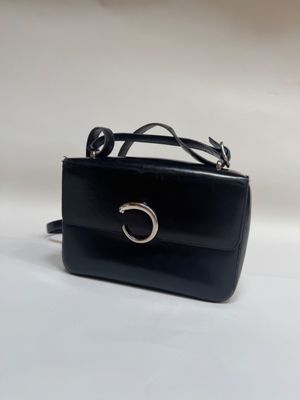 Le petit sac à main noir est muni d'un anneau métallique sur la poignée.