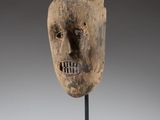 un masque en bois posé sur un socle, devant un fond gris