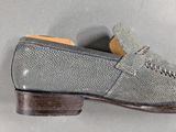 grey leather loafer shoes with brown soles on a gray surface