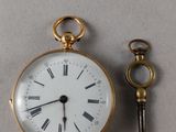 une petite montre de poche en or et une clé posées sur une table