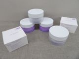 quatre flacons de produits de soin pour la peau, blancs et violets, posés sur une table