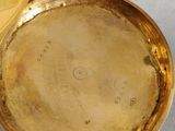 a gold pocket watch sitting on a table next to a coin