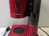 red and black coffee maker sitting on top of a table next to a charger