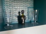 des bouteilles et des verres posés sur une étagère dans une pièce recouverte de papier peint