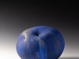 une pomme bleue posée sur une surface blanche