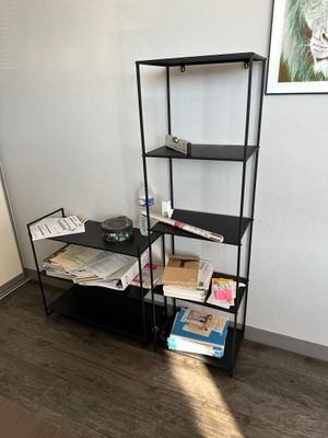 une étagère noire sur laquelle sont posés des livres, dans un coin de la pièce