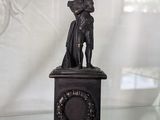 une statue représentant un homme tenant une horloge posée sur une table en verre