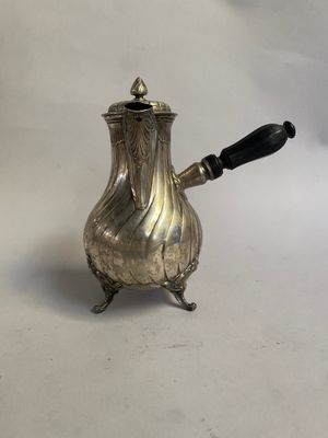 une cafetière en argent avec une poignée noire, posée sur une surface blanche