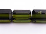un gros plan sur trois perles de tourmaline verte posées sur une surface blanche