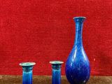 trois vases bleus posés sur une table près d'un mur rouge