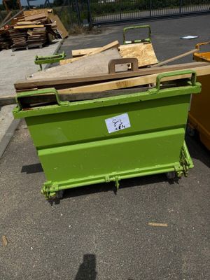 une benne verte posée sur un parking, à côté d'un tas de bois