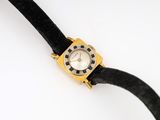 a gold watch with a black band on a white surface