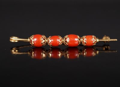a gold and coral bead broochle on a black surface
