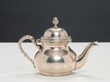 une théière ancienne en argent avec son couvercle, posée sur une table blanche