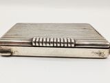 un petit étui à cigarettes argenté, muni d'une poignée en métal sur un fond blanc