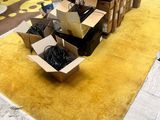 un tapis jaune posé à même le sol, sur lequel se trouvent des cartons