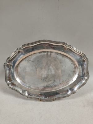 une assiette ancienne en argent sur fond blanc, ornée d'une petite fleur