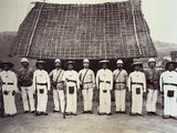 a group of men standing in front of a thatched roof