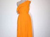une robe orange posée sur un mannequin, devant un mur blanc