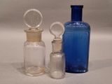 three glass bottles and a glass stopper on a white surface