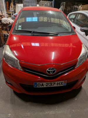 the red toyota yaris is parked in a garage with other cars in the background