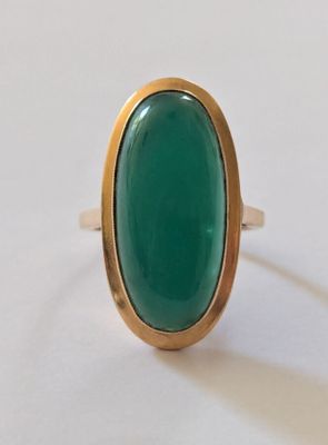 une image représentant une bague en pierre verte posée sur une surface blanche