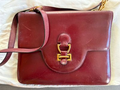 un sac à main rouge orné d'une boucle dorée, posé sur un drap blanc