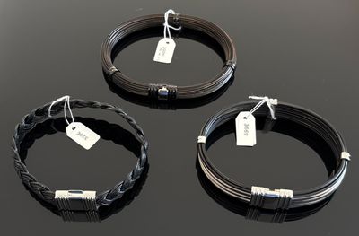trois bracelets en fil métallique noir, munis d'étiquettes, posés sur une surface noire