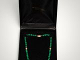 a green beaded necklace in a black box with a gold clasp