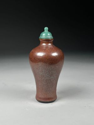un vase marron avec un couvercle vert posé sur une surface blanche