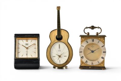 three different clocks and a guitar on a white background