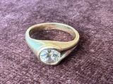 une bague en or sertie d'un diamant, posée sur un fond violet