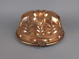 an antique copper plate with a domed lid on a gray surface