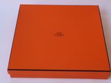une boîte orange ornée d'un logo, posée sur une surface blanche