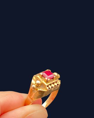 someone is holding a gold ring with a pink stone in it