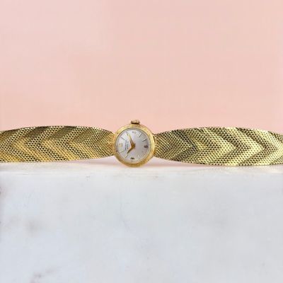 une montre-bracelet en or avec un cadran blanc posée sur une surface en marbre