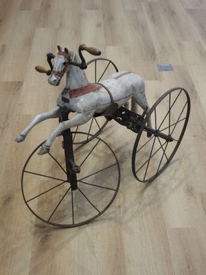 un cheval en peluche monté sur un tricycle posé sur un parquet