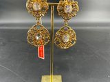 a pair of earrings on a gold stand with a red and white flag