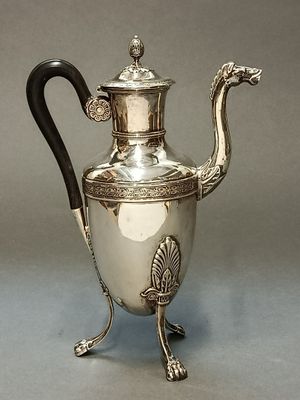 une théière en argent avec une anse noire, posée sur un socle