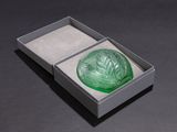 a green glass object in a box on a black surface