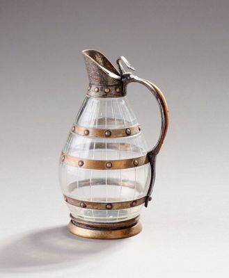 une image représentant un pichet en verre muni d'une anse en métal, posé sur une surface blanche