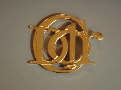 une broche en or sur laquelle figure la lettre « d »
