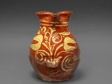 un vase rouge orné de motifs dorés sur un fond gris