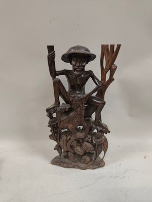 figurine en bois sculptée représentant un homme assis sur une souche d'arbre, coiffé d'un chapeau et muni d'une canne