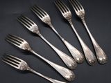 six silver forks with ornate designs on them on a black surface