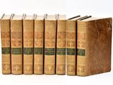 six old books are lined up in a row on a white surface