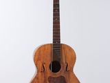 an old wooden guitar hanging from a string on a white wall