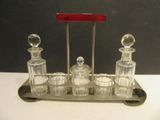 un plateau en argent avec quatre carafes en verre et une poignée rouge