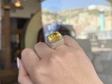 woman ' s hand holding a yellow diamond ring in front of a window