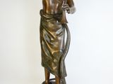 statue en bronze représentant une femme tenant un serpent, posée sur un socle en bois